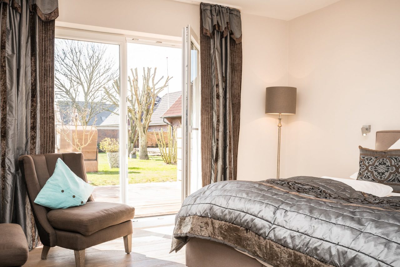 Modernes Doppelzimmer mit Doppelbett, zwei Sesseln, Willkommensgetränken und Terrasse mit Blick in den Garten im Landhaus Sylter Hahn.