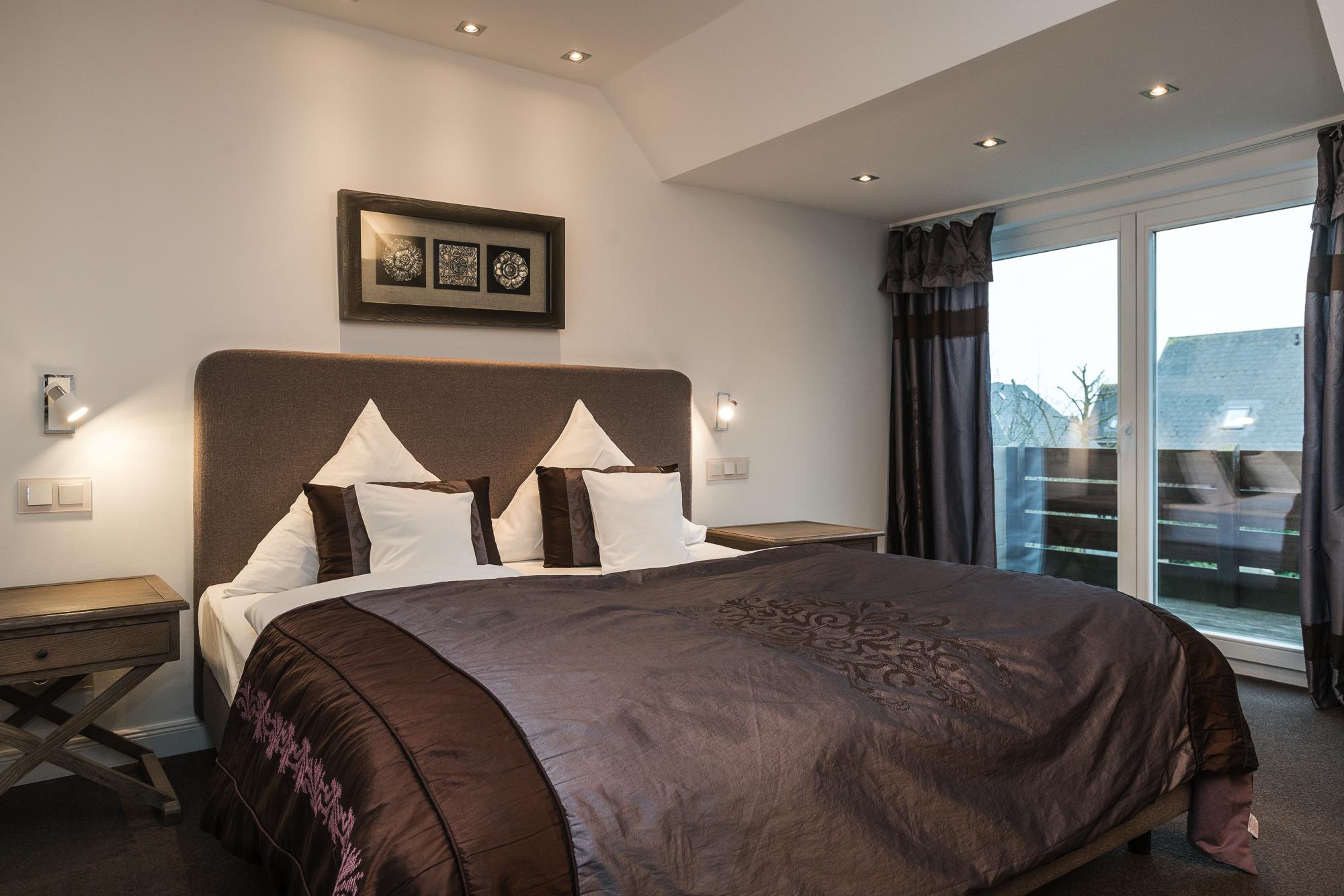 Modernes Doppelzimmer mit Doppelbett, zwei Holznachttischen und Balkon im Hotel Landhaus Sylter Hahn in Westerland.