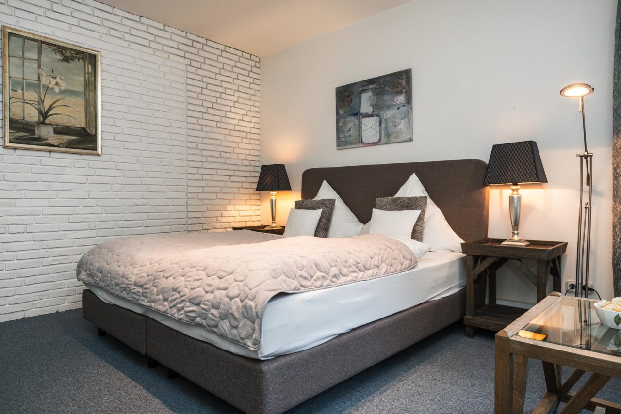 Doppelzimmer mit Doppelbett und zwei Holznachttischen mit Leselampen im Hotel Landhaus Sylter Hahn in Westerland auf Sylt.