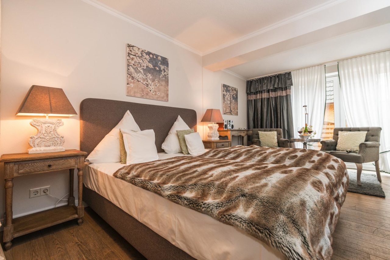 Modernes Doppelzimmer mit Doppelbett, zwei Sesseln und zwei Nachttischen aus Holz im Hotel auf Sylt Landhaus Sylter Hahn.
