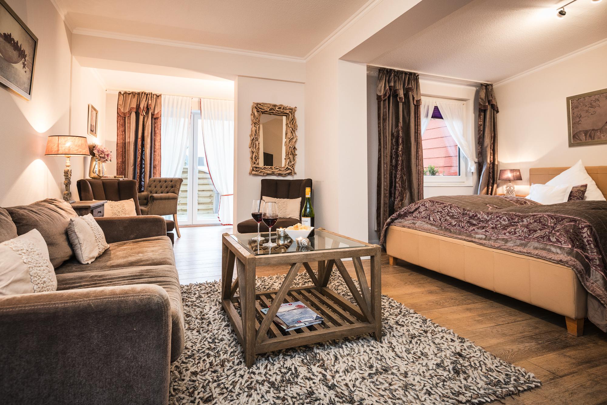 Doppelzimmer mit einem gemütlichen Sofa, Leselampe und Willkommensgetränken im Hotel Landhaus Sylter Hahn in Westerland auf Sylt.